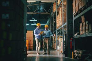 two men wearing hard hats talking in a factor